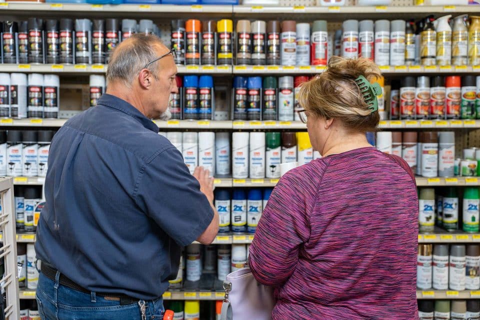 A Caucasian male employee at Witt Do it Best in Sturgis, MI assisting a female customer deciding what kind of spray paint she wants to purchase.