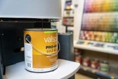 A can of yellow-labeled paint sitting on a white counter ledge with paint samples hanging in the background at Witt Do it Best's Sturgis location.